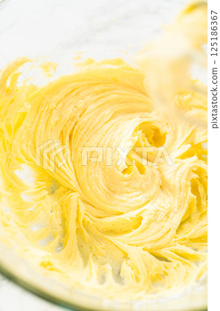 A smooth and fluffy mixture of butter and sugar is perfectly creamed in a glass mixing bowl, forming the base for lemon spritz cookie dough. The light, whipped texture ensures a soft, melt-in-your 125186367