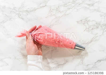 A piping bag filled with vibrant cranberry buttercream, ready for decorating lemon spritz cookies. The smooth buttercream is prepared for precise and beautiful decoration with a star tip nozzle. 125186398