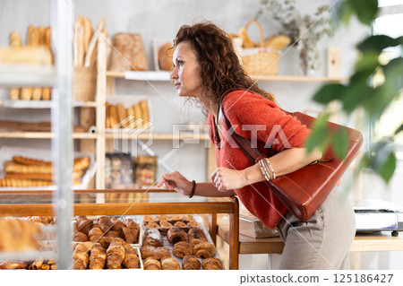 European woman near window of bakery food court store examines assortment European woman near window of bakery food court store examines assortment 125186427