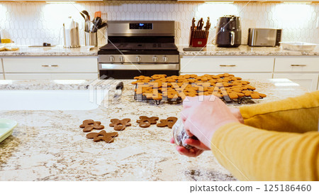 Using various festive cookie cutters, we're cutting out charming gingerbread cookies from the rolled dough on the sleek marble counter, bringing holiday cheer to the modern kitchen. 125186460