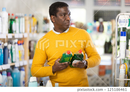 Male shopper selects dishwashing sponges in the household goods section of supermarket 125186461
