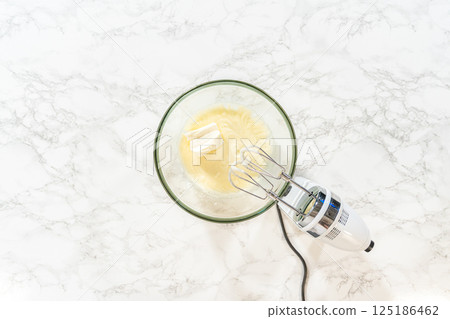 A hand mixer is used to combine eggs and other ingredients in a glass bowl, preparing for baking. A hand mixer is used to combine eggs and other ingredients in a glass bowl, preparing for baking. 125186462