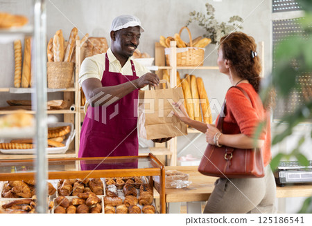 Man baker giving paper bag with pastry to female customer Man baker giving paper bag with pastry to female customer 125186541