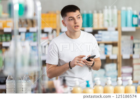 Young man with phone is shopping in pharmacy 125186574