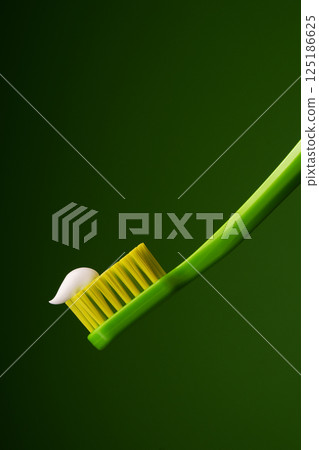Green plastic toothbrush with white toothpaste on a green background. Oral health. Green plastic toothbrush with white toothpaste on a green background. Oral health. 125186625