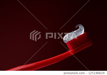 Red plastic toothbrush with transparent toothpaste on a dark red background. Dentistry. Red plastic toothbrush with transparent toothpaste on a dark red background. Dentistry. 125186629