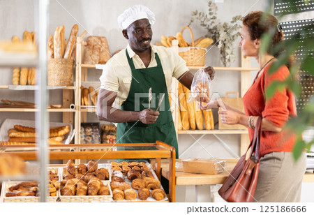 Baker places fresh croissants in plastic bag for female customer Baker places fresh croissants in plastic bag for female customer 125186666