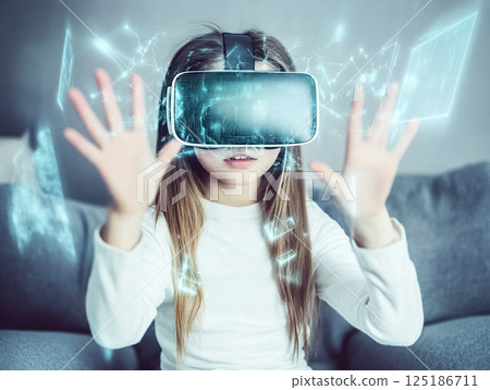 A young girl wearing a virtual reality headset, interacting with a digital environment. Her hands are raised as if engaging with virtual objects, while futuristic graphics surround her, creating an 125186711