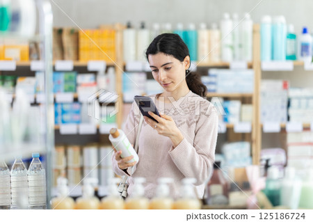 Girl in autumn clothes scans code on medicinal shampoo to check expiration date 125186724