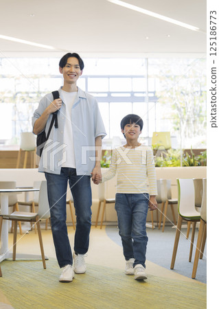 Father and son walking hand in hand: A father in his 30s and a 9-year-old boy Father and son walking hand in hand: A father in his 30s and a 9-year-old boy 125186773
