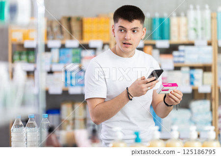 Attentive young guy client choosing box of paracetamol antipyretic pills, scan QR code on label, looking at composition of medicine in drug store Attentive young guy client choosing box of paracetamol antipyretic pills, scan QR code on label, looking at composition of medicine in drug store 125186795
