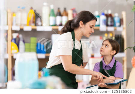 Woman seller with daughter, using paper report make inventory in store. Woman seller with daughter, using paper report make inventory in store. 125186802