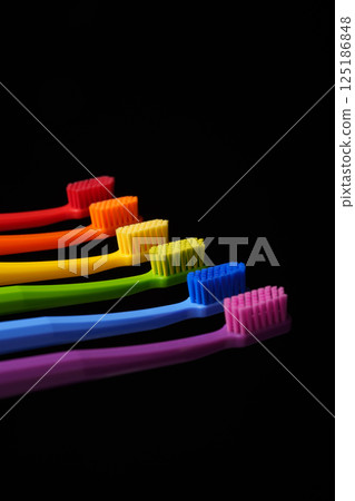 Multicolored plastic toothbrushes on a black background. Banner for dentistry. Colors of the rainbow. 125186848