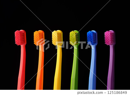 Multicolored plastic toothbrushes on a black background. Banner for dentistry. Colors of the rainbow. 125186849