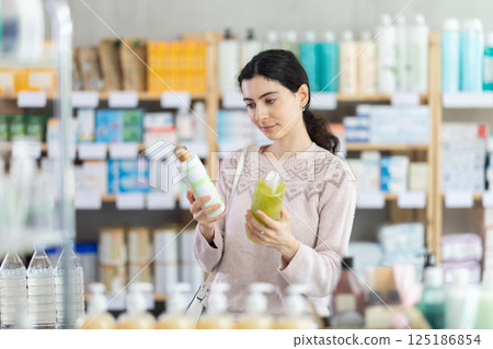 Female shopper in autumn clothes chooses medicated shampoo at pharmacy Female shopper in autumn clothes chooses medicated shampoo at pharmacy 125186854