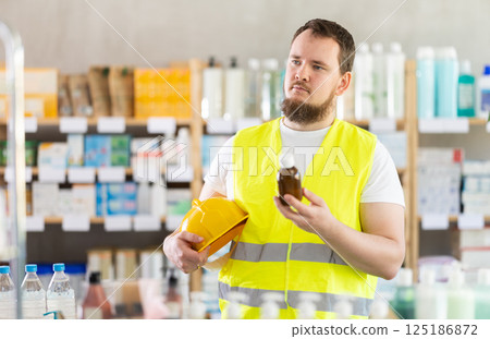Young man builder chooses syrup at pharmacy Young man builder chooses syrup at pharmacy 125186872
