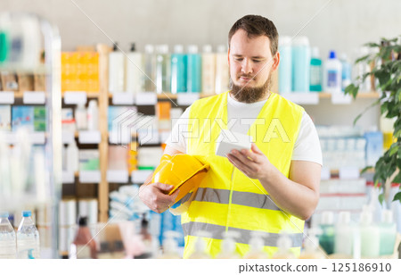 Male builder in yellow vest with helmet in his hands looks for medicine in pharmacy 125186910