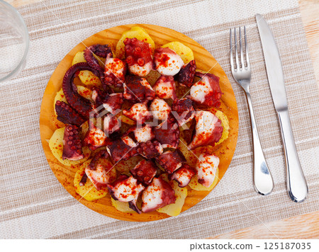 Chopped cooked octopus tentacles with smoked paprika and potato on wooden board 125187035