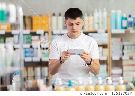 Portrait of handsome young guy holding and choosing box with best pills to improve well-being in pharmacy 125187037