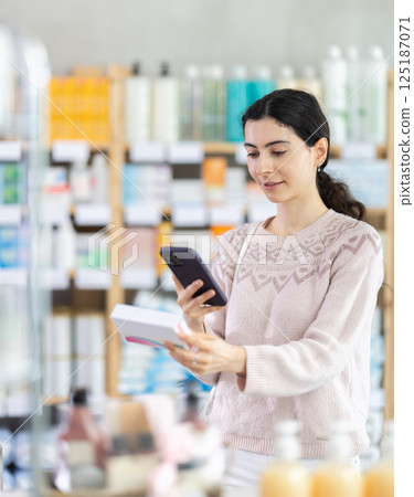 woman is standing in a pharmacy and scanning the barcode of a box of pills 125187071