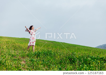 woman standing with her arms outstretched in a field of flowers in spring 125187163