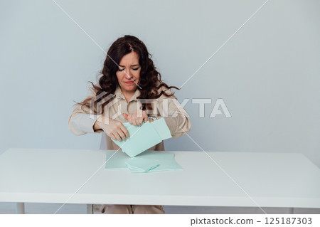 woman tearing paper while sitting at white office desk woman tearing paper while sitting at white office desk 125187303