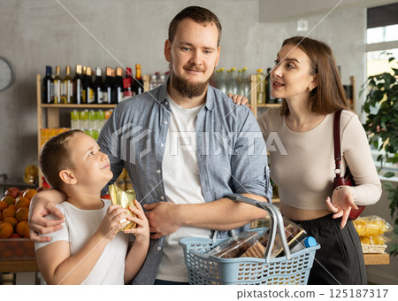 Family with various products in hands continuing shopping in grocery department of supermarket 125187317