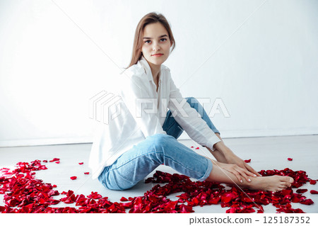 Beautiful woman sitting on the floor with red rose petals 125187352