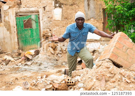 Upset african american man and destroyed house after earthquake 125187393