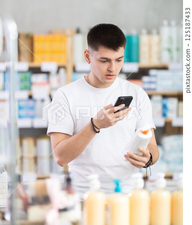 Guy in pharmacy scans QR code on emollient cream 125187433