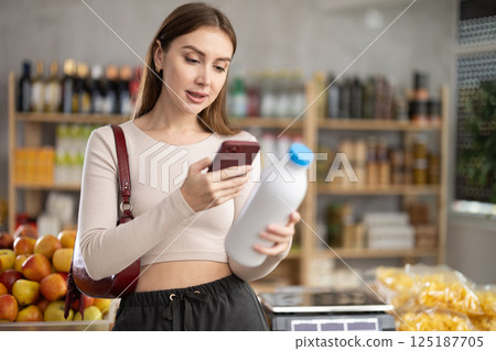 Female buyer checks suitability - scans QR code on bottle of milk label in grocery store Female buyer checks suitability - scans QR code on bottle of milk label in grocery store 125187705