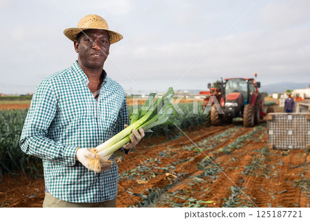 African american man with a leek in hand in field African american man with a leek in hand in field 125187721