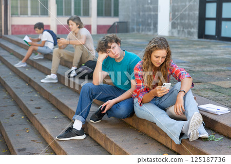 Girl and boy write messages on smartphone on street 125187736