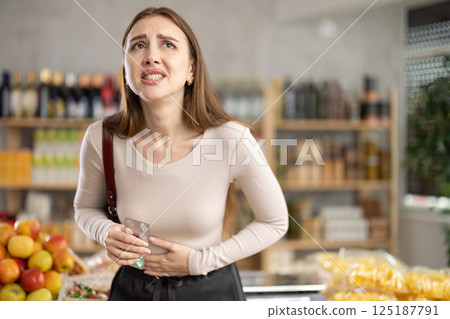 Woman develops stomach ache while grocery shopping in supermarket 125187791