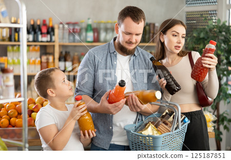 Couple of man and woman with boy choosing juices in grocery Couple of man and woman with boy choosing juices in grocery 125187851