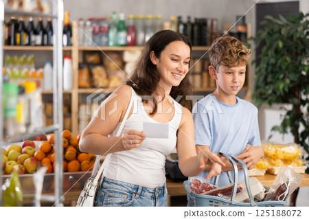 In store near snack display case, mom and son stand with paper list, recall planned products In store near snack display case, mom and son stand with paper list, recall planned products 125188072
