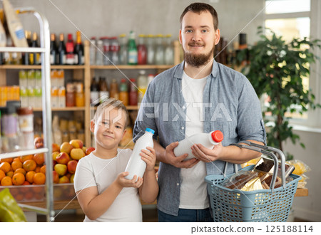Preteen boy with father choosing bottled milk in grocery store 125188114