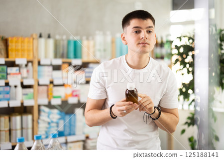 Young man buyer selects expectorant syrup Young man buyer selects expectorant syrup 125188141