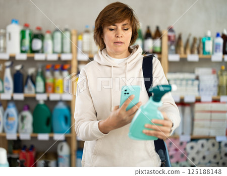 Woman client scans QR code on package and downloads promo code to purchase bathroom cleaner spray 125188148