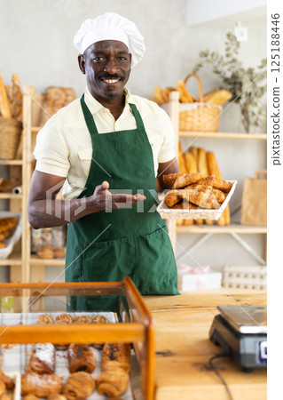 Smiling baker offers to buy fresh hot croissants 125188446