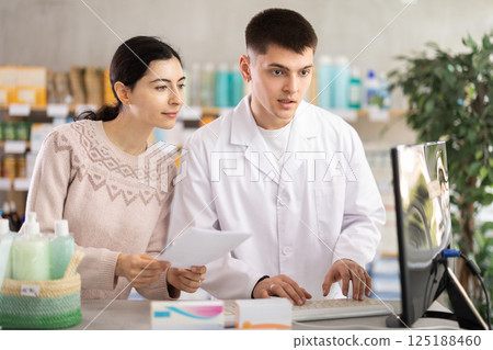 Male pharmacist helps girl buy medicine - he reads the prescription and compares it with data on computer 125188460