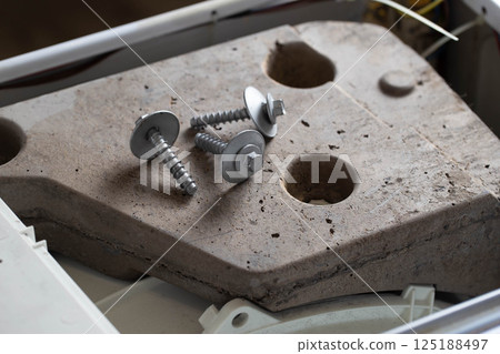 Bolts and tools lie on the counterweight of the washing machine. Concept of noise, vibration and rumble due to an unscrewed counterweight, industry Bolts and tools lie on the counterweight of the washing machine. Concept of noise, vibration and rumble due to an unscrewed counterweight, industry 125188497