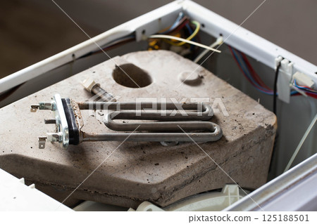 The electric heating element and temperature sensor, thermostat are on the disassembled washing machine. The concept of replacing and repairing spare parts in a washing machine. Scale and hard water 125188501