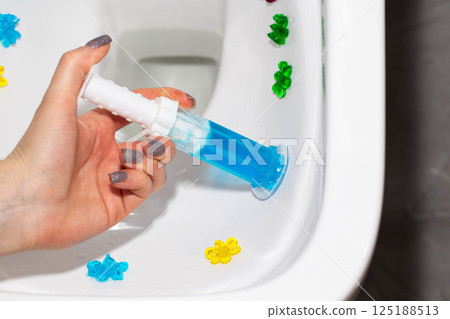 A syringe with ocean-scented gel for cleaning and disinfecting the toilet in a hand against the background of a toilet. Antibacterial effect, close-up A syringe with ocean-scented gel for cleaning and disinfecting the toilet in a hand against the background of a toilet. Antibacterial effect, close-up 125188513