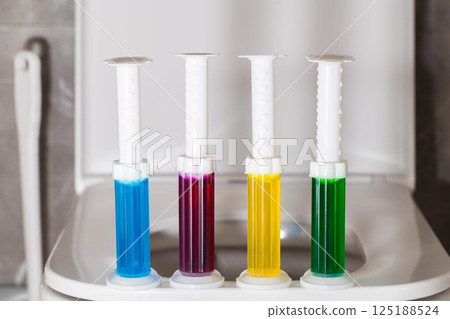 A set of multi-colored syringes with different scents on the toilet bowl in the toilet for cleaning and disinfection. Hygiene and antibacterial effect, close-up A set of multi-colored syringes with different scents on the toilet bowl in the toilet for cleaning and disinfection. Hygiene and antibacterial effect, close-up 125188524