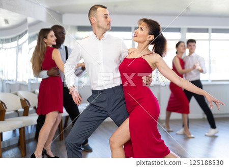 Smiling young woman in red dress and partner successfully perform mesmerizing movements of paso doble dance during dance party 125188530