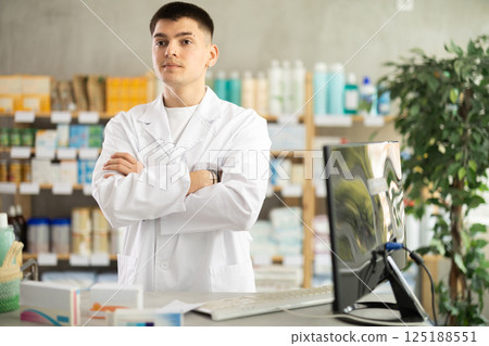 Young man pharmacist standing and posing near counter in pharmacy 125188551