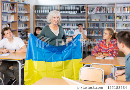 Mature female teacher shows scholchildren the national flag of Ukraine 125188584