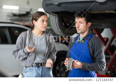 Male auto mechanic discussing with woman the cost and time to repair her car at car service Male auto mechanic discussing with woman the cost and time to repair her car at car service 125188587