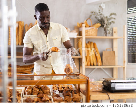 Man putting croissants into plastic bag in bakery Man putting croissants into plastic bag in bakery 125188688